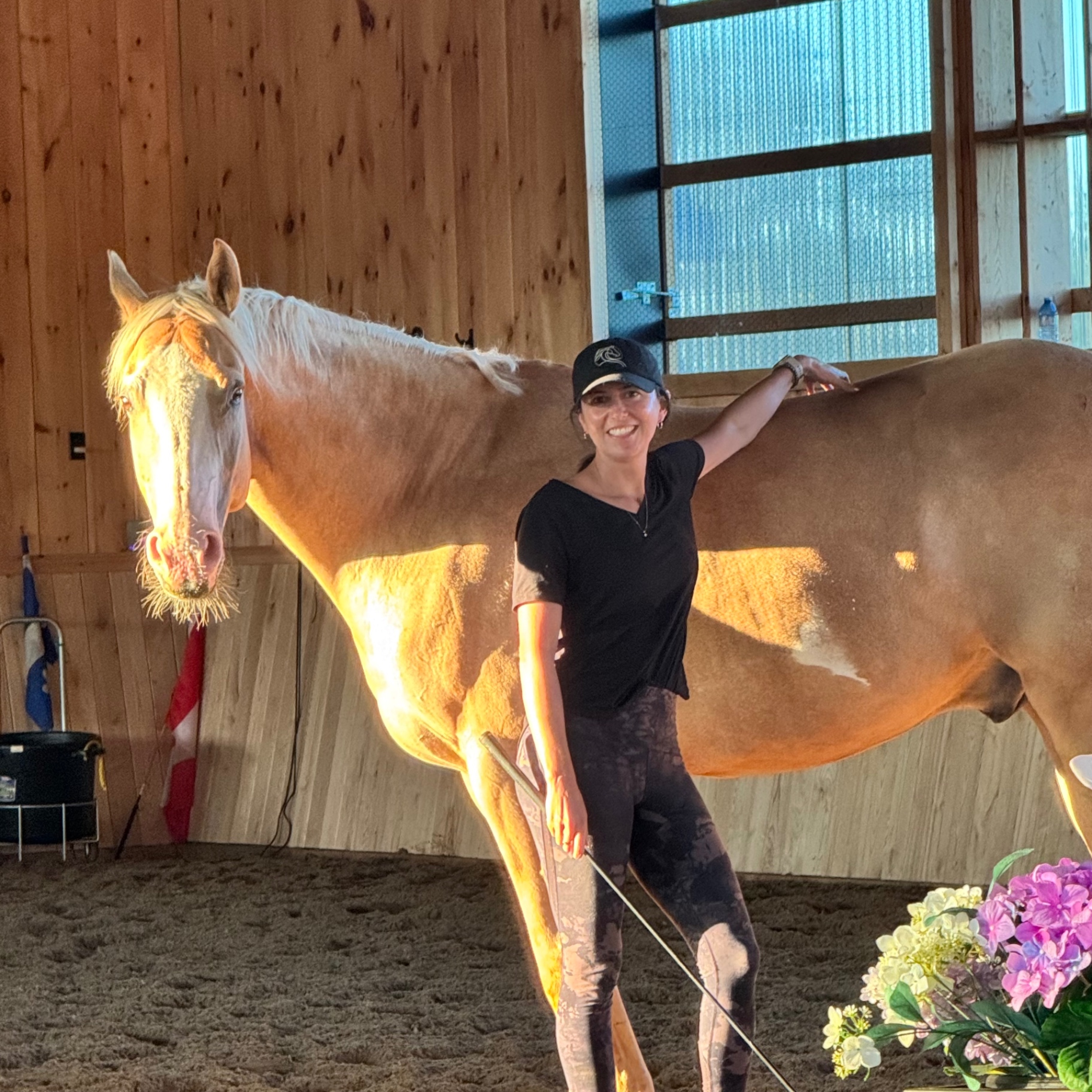 Jillian Nielsen standing beside her palomino horse in a sunlit indoor arena